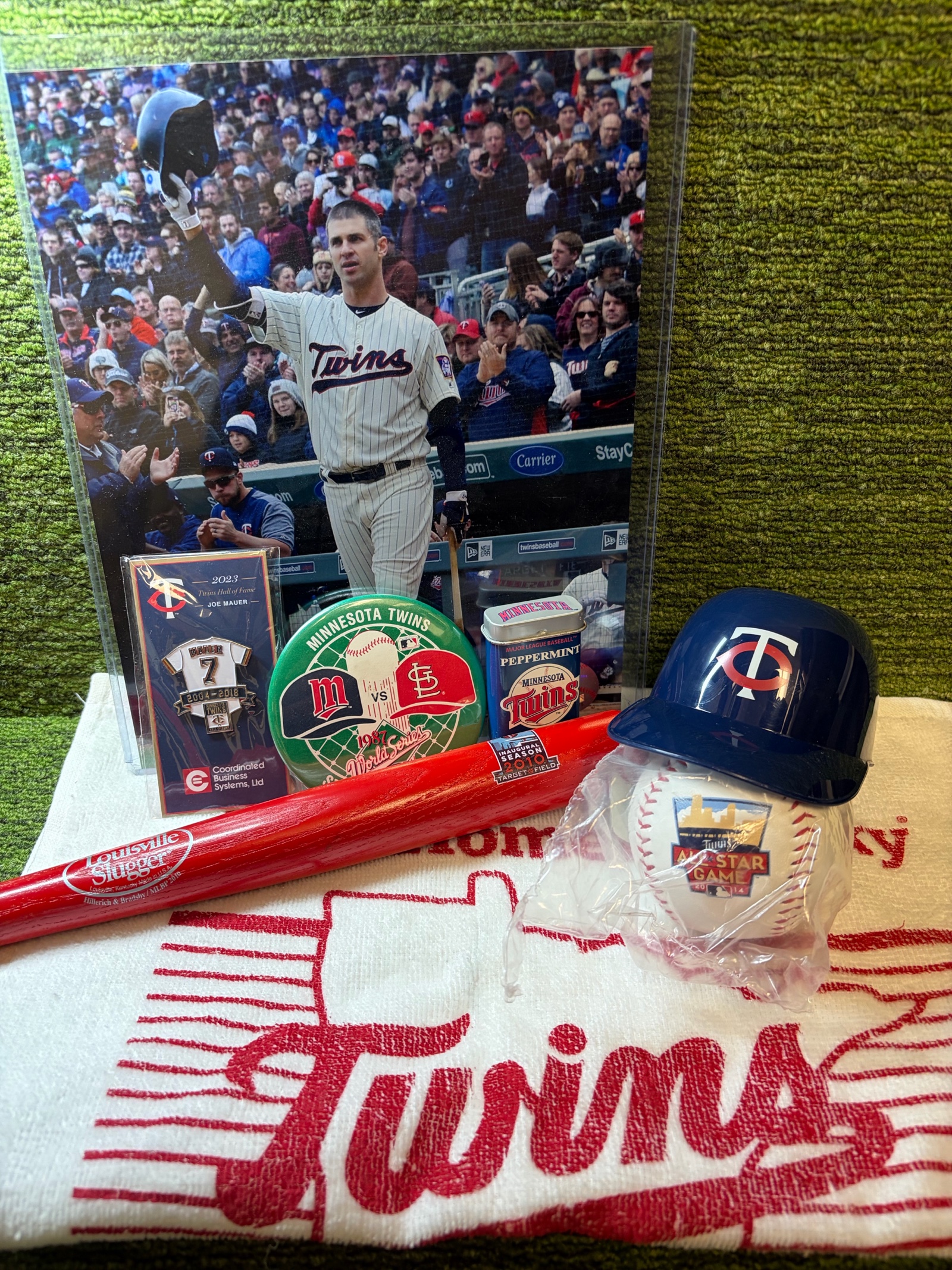 lot 64 image: Minnesota Twins Memorabilia Package 2010 Inaugural Season Mini Louisville Slugger, 2014 ALL-STAR Game Ball, Chewing Gum Tin Holder(2004), 2020 Towel Homer Hankie, & Joe Mauer Pin and Photo, & mini Helmet