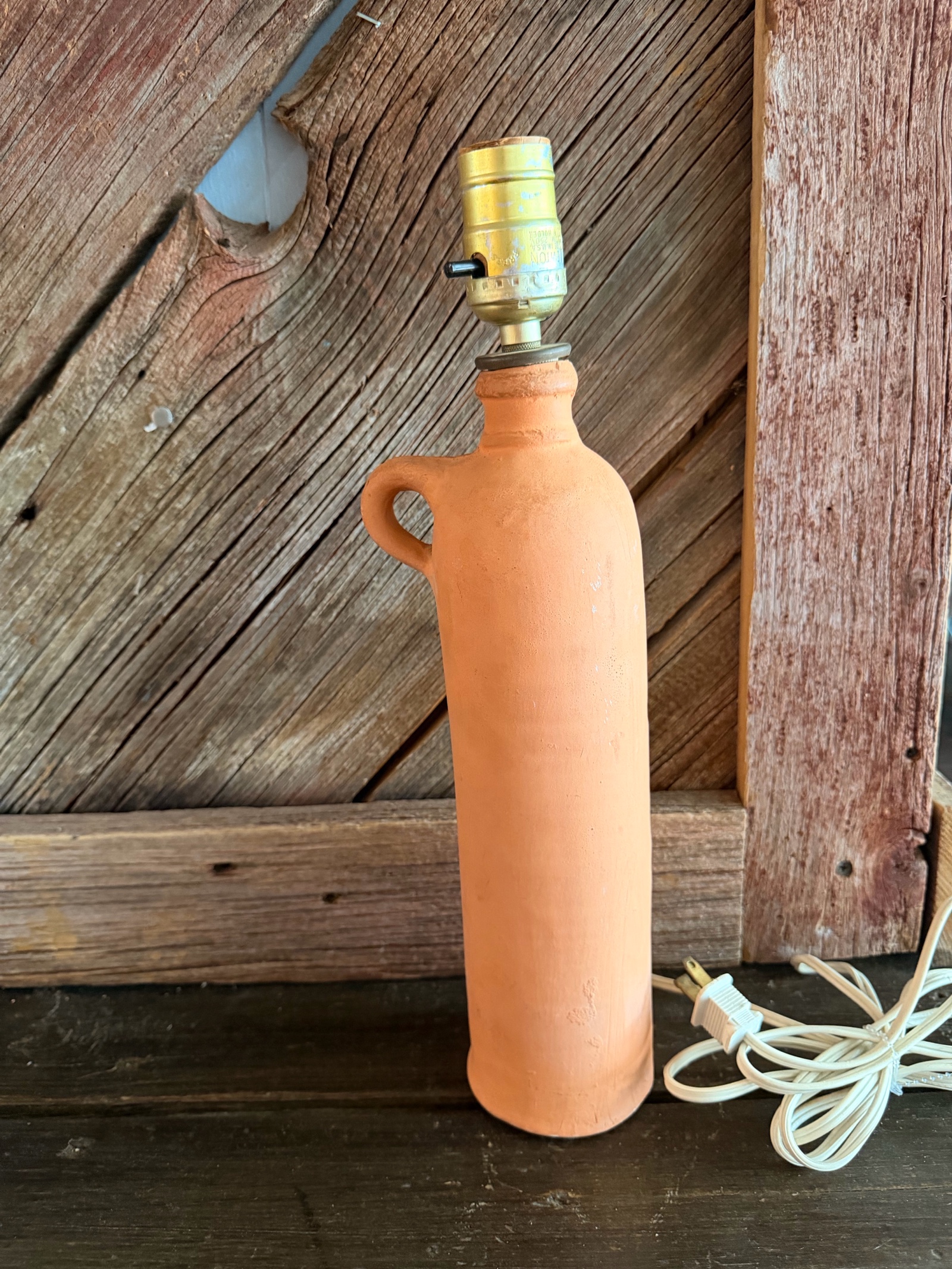 terracotta ceramic bottle lamp featuring a curved handle.