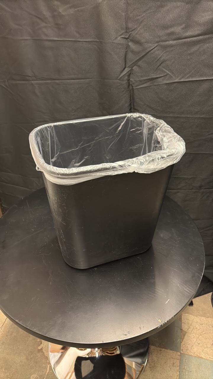 Black Plastic Garbage Can About One and a Half Feet in Height, Comes With Roll of Garbage Bags